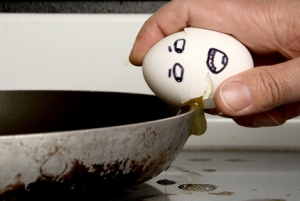 Egg with face being cracked on frying pan