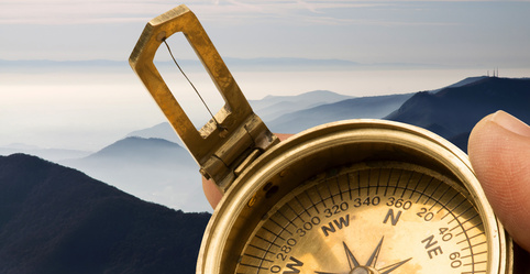 Old fashioned brass compass held in hand, against background of mountains and clouds.