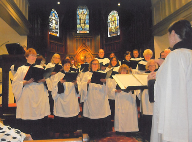 Episcopal choir in black robes and white cottas, on dais, holding music folders